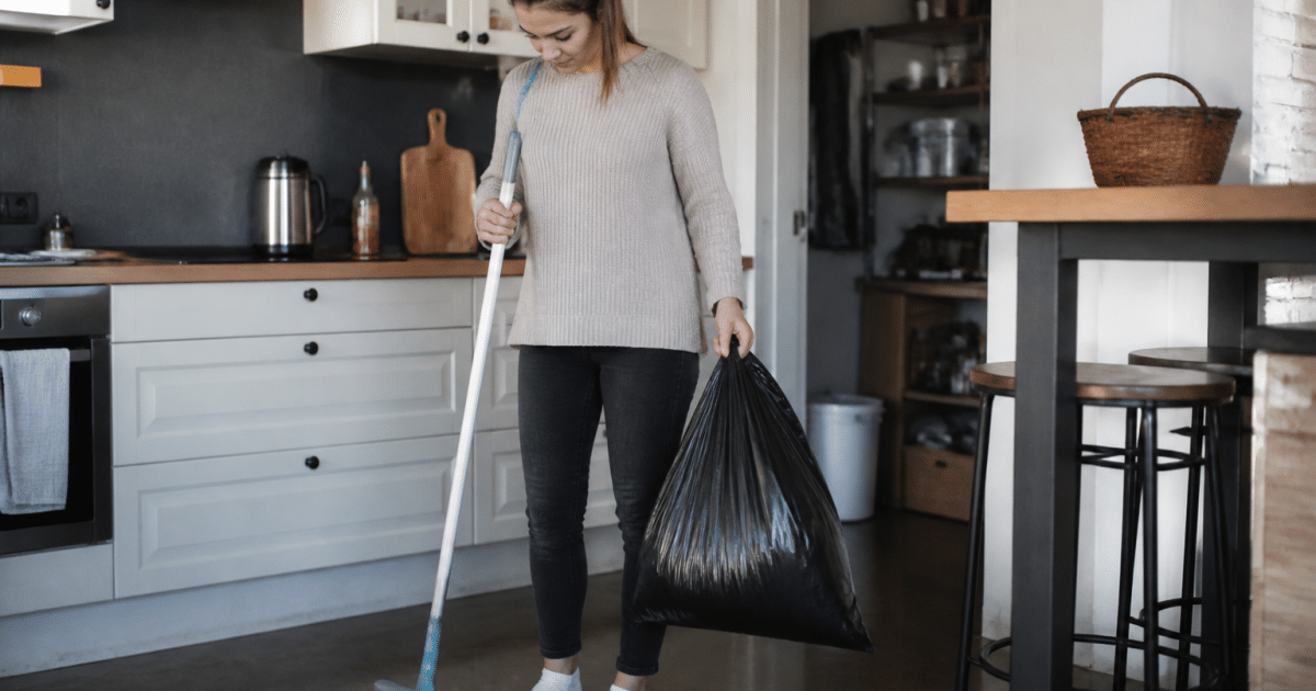 Personne tenant balai et sac poubelle dans cuisine