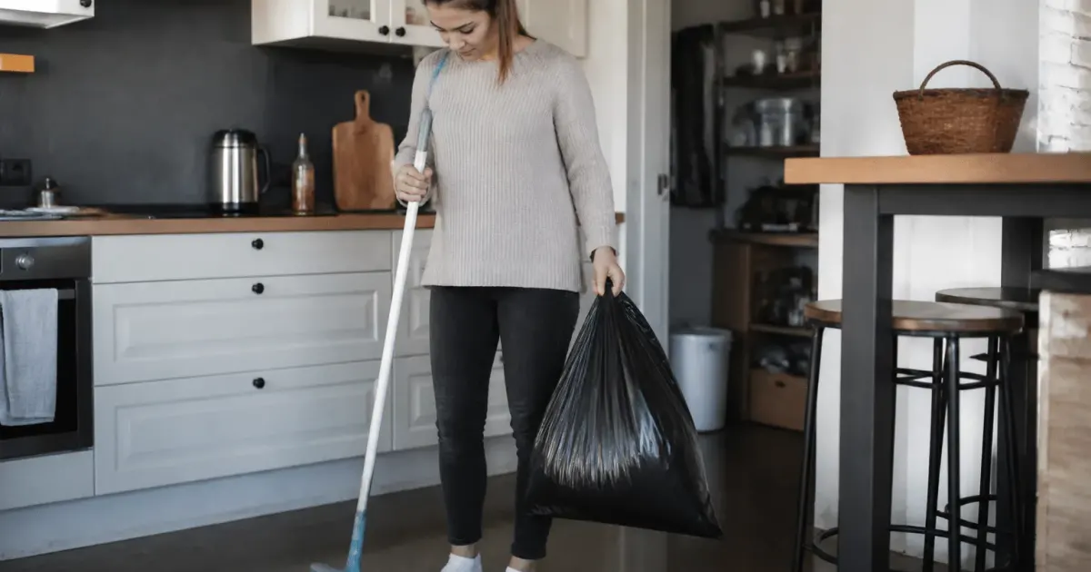 Personne tenant balai et sac poubelle dans cuisine