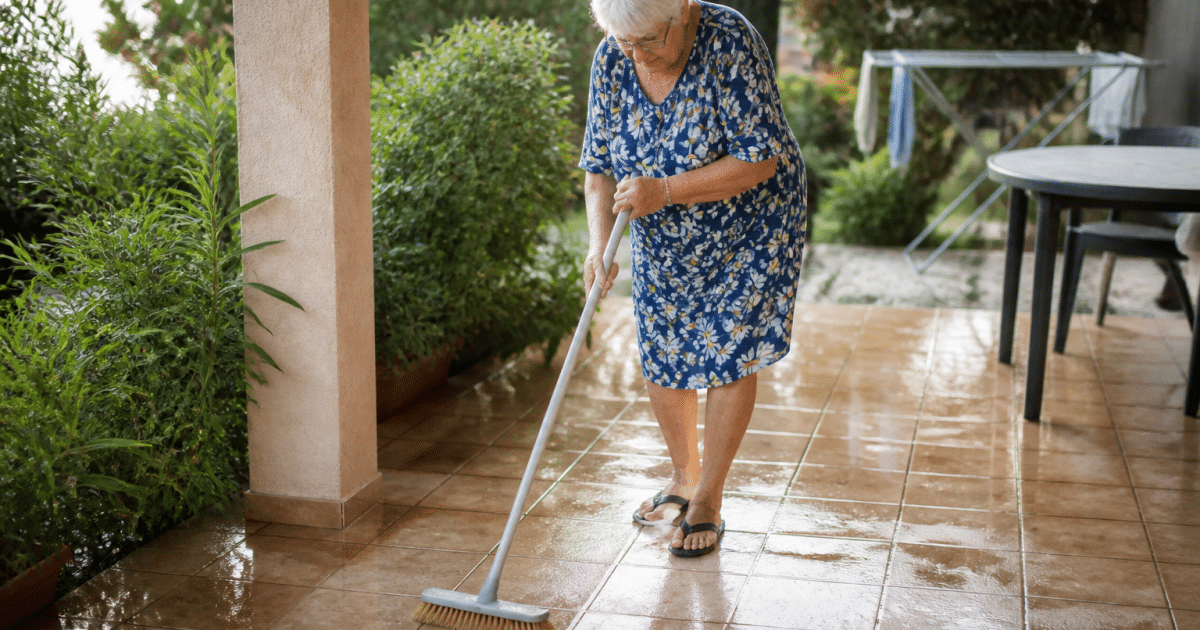 Femme agee frotte carrelage terrasse avec balai brosse