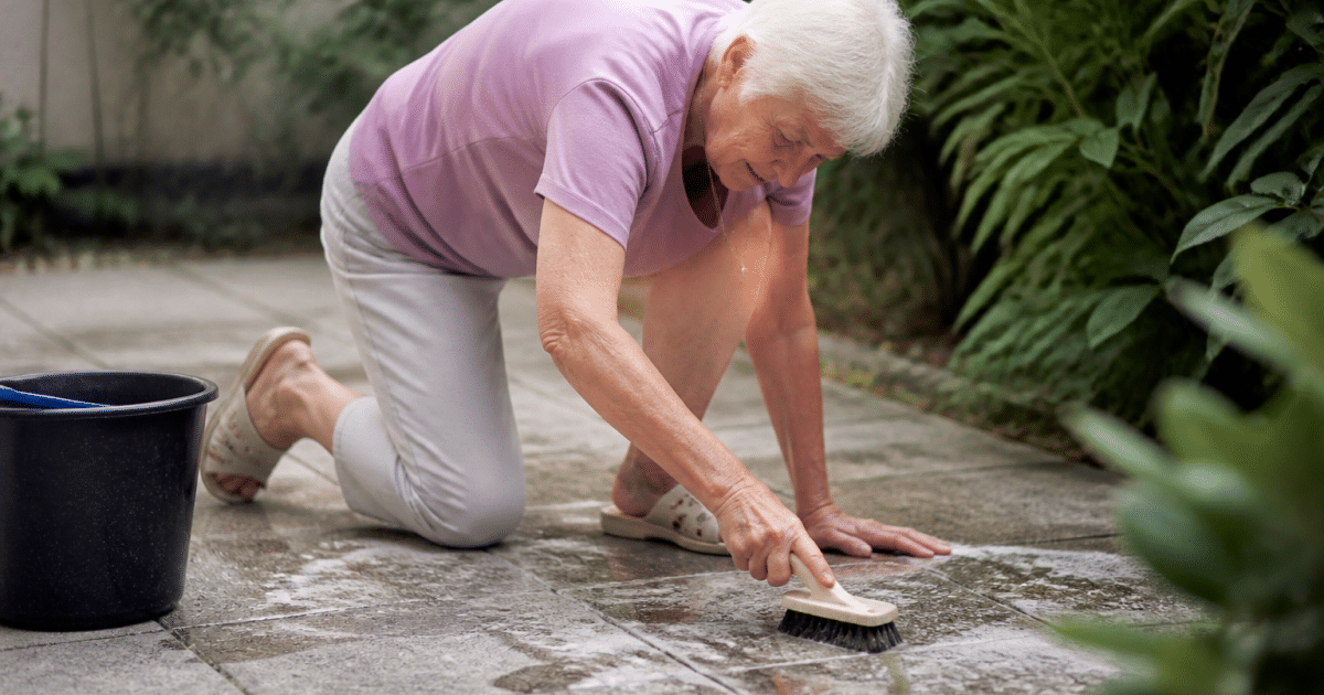 Femme agee frottant dalles grises terrasse avec brosse dure