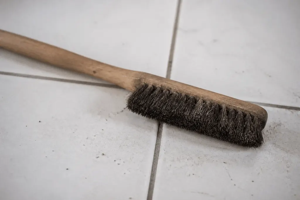 Brosse poussiereuse sur carrelage blanc avec joints gris