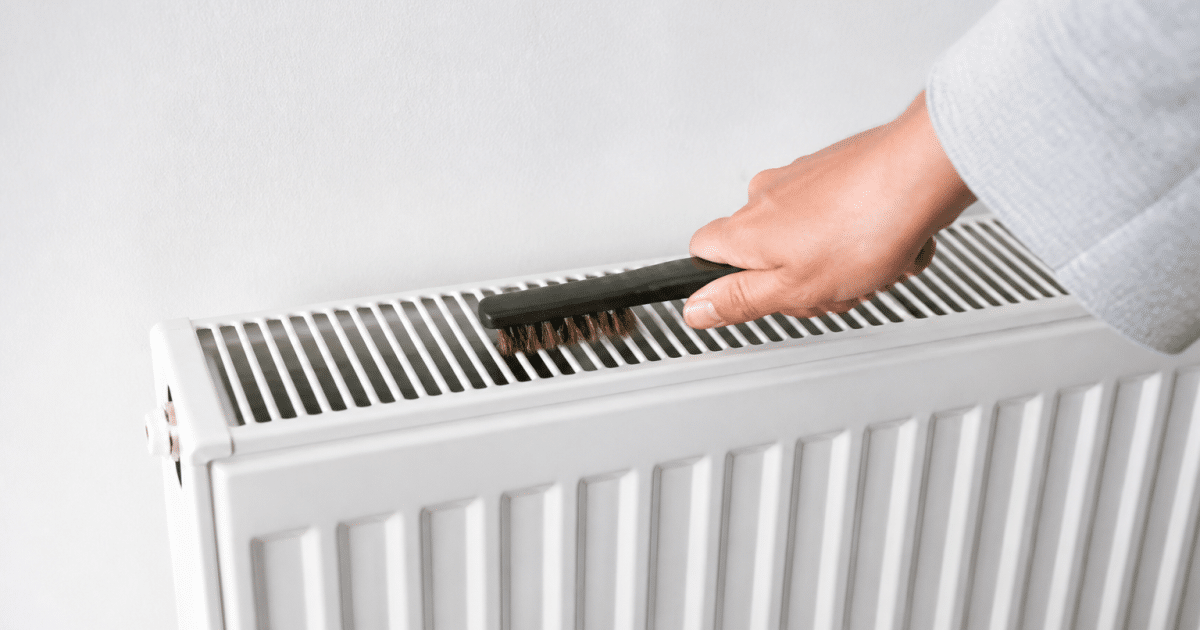 Personne tenant brosse devant radiateur blanc avec grille