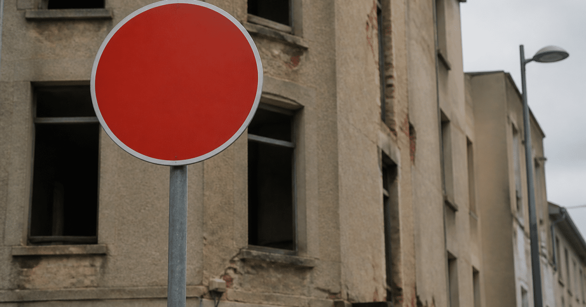 Panneau routier rouge avertissant devant immeubles urbains délabres