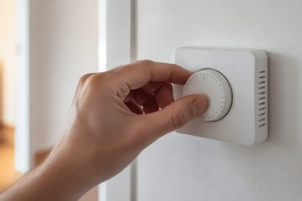 Main de personne ajustant cadran thermostat blanc mural