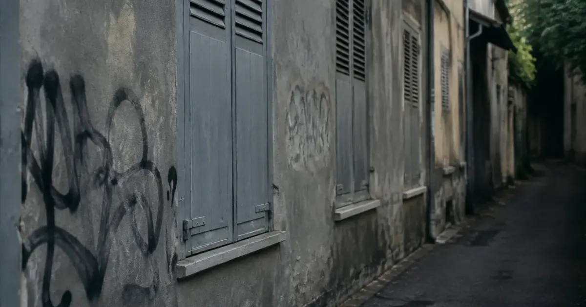 Facade grise avec tags, volets fermes sur ruelle sombre